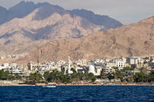 Seaside view of the jordan city of Aqaba at the Red Sea. Deep blue sea, white buildings, green trees and majestic hills.