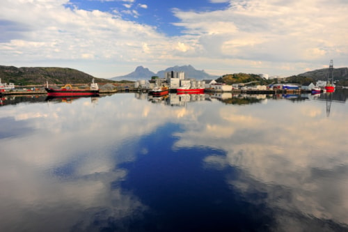 Summer, blue sky, cloud reflections. Industrial port of Bodo, Norway showing ships and herring oil production plant. 