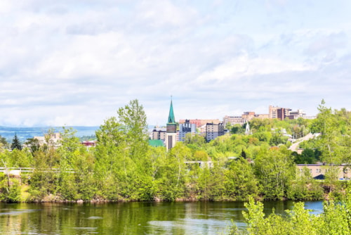 Cityscape or skyline of Saguenay, Canada city in Quebec in summer with church spire, many houses, buildings and green park trees