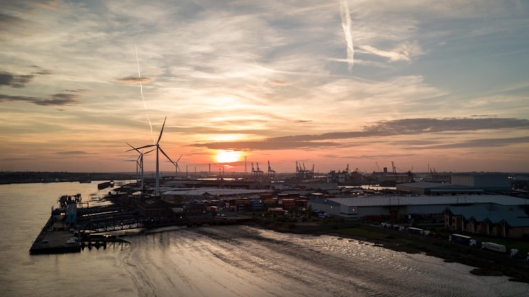 Sunset at the Port of Tilbury, Essex, UK. Aerial drone view of the port of Tilbury in Essex, England, with wind turbines and cranes dominating the skyline.